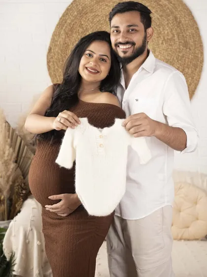 A happy couple holding up a tiny baby onesie. This is a classic and joyful way to announce their excitement for the new arrival.