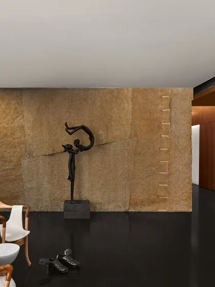 A passage in the Baid Residence designed as a gallery. It features designer chairs from Giorgetti, a stone-clad wall, and a black Radha Krishna sculpture, creating a journey through art and design.