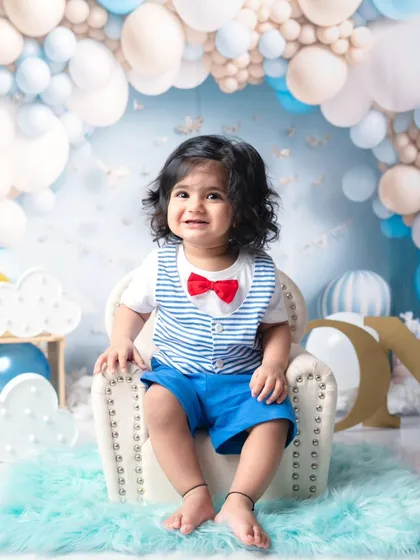 Dressed up and ready to party. This little gentleman with his red bow tie is all smiles for his first birthday photoshoot, surrounded by a sea of blue balloons.