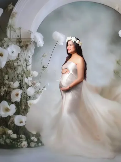 An ethereal vision in a misty, floral wonderland. This setup uses a white floral arch and soft fog to create a dreamy and romantic atmosphere for a truly magical maternity portrait.