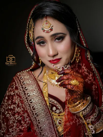 A classic bridal portrait of the beautiful Afsana. The lighting highlights the rich details of her red and gold wedding attire and her intricate jewelry.