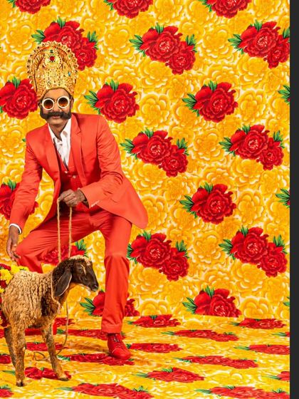 Cop Shiva in a matching red suit, continuing the performative narrative with the lamb. This image showcases the artist as an active participant in the surreal worlds he constructs.