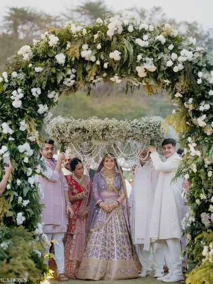 The bride's entrance under a beautiful floral phoolon ki chaadar. Riti's serene expression as she walks towards the mandap, surrounded by her loved ones, is a classic and heartwarming wedding moment.
