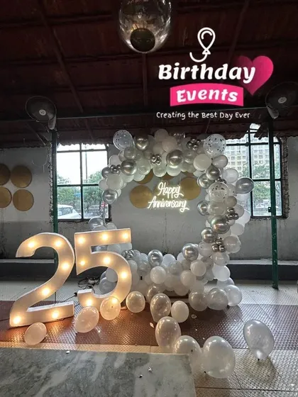 This 25th anniversary setup was designed for a restaurant or event space. A classic silver and white balloon arch frames the "Happy Anniversary" sign, with the large marquee numbers making a bold statement.