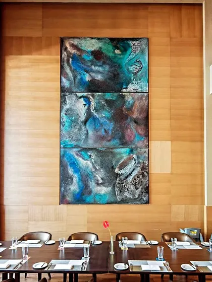 'Feast' by Adil Writer, a triptych of acrylic and clay on wood, displayed in a dining room at the Sheraton. The piece celebrates Parsi artistry with motifs from Bidriware artifacts.