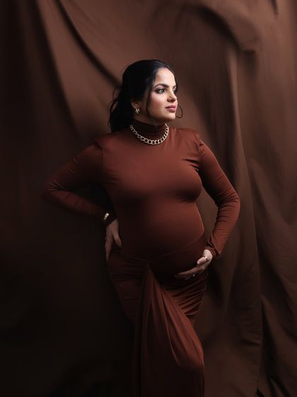 A portrait of pure confidence and style. This mom-to-be looks absolutely stunning in a chic brown gown, showcasing a more glamorous and high-fashion look in the studio.