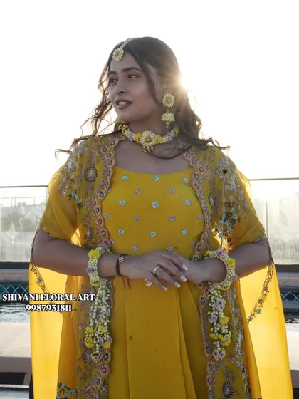 A sun-kissed photo of a bride on her Haldi day. She is wearing a yellow floral choker, maang tikka, and hand jewellery that I designed to match her outfit perfectly.