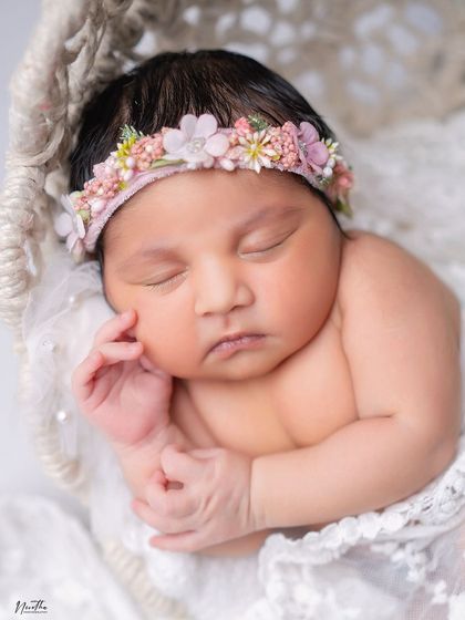 A close-up portrait of a sleeping newborn, adorned with a delicate floral headband and wrapped in soft lace.