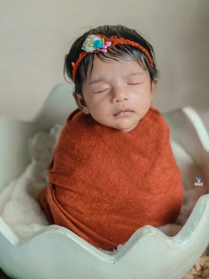 A close-up of the newborn in the eggshell prop, showing the delicate details of the wrap and headband.