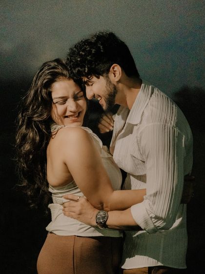 A candid photo filled with genuine laughter and affection. The dark, natural background makes the couple's bright smiles and connection the absolute focus of the image.