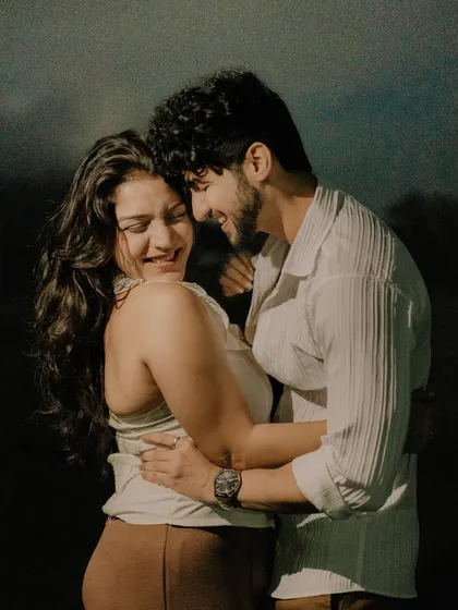 A candid photo filled with genuine laughter and affection. The dark, natural background makes the couple's bright smiles and connection the absolute focus of the image.