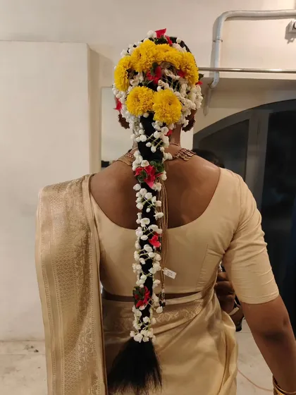 A stunning example of a traditional South Indian bridal braid, or 'poola jada'. This intricate hairstyle is heavily decorated with fresh jasmine and marigold flowers, creating a fragrant and visually spectacular look.