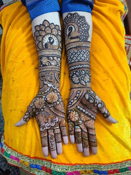 A beautiful example of asymmetrical bridal mehendi. One arm features a prominent peacock and lotus design, while the other has a more floral-focused pattern, creating a unique and balanced look.