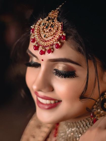 A close-up profile shot of the bride, highlighting her flawless makeup, intricate maang tikka, and elegant earrings. Her gentle smile completes this stunning portrait.