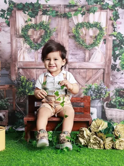 A happy toddler sits in front of a rustic garden gate setup. This theme combines natural greenery with charming props for a secret garden feel.
