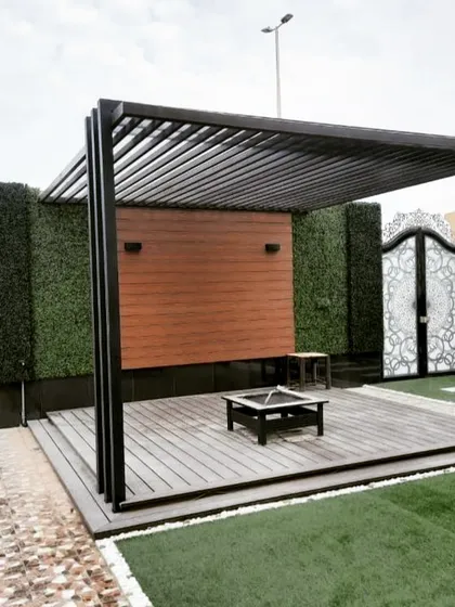 A functional outdoor space featuring a pergola with a wood-paneled accent wall and a fire pit. The design is flanked by artificial green walls and an ornate gate, creating a private courtyard feel.