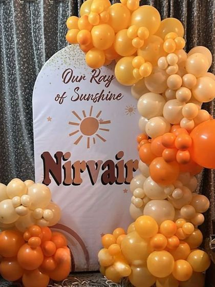 A 'Ray of Sunshine' themed birthday party. This warm and cheerful setup features a custom arched backdrop and a beautiful balloon garland in shades of orange and yellow.