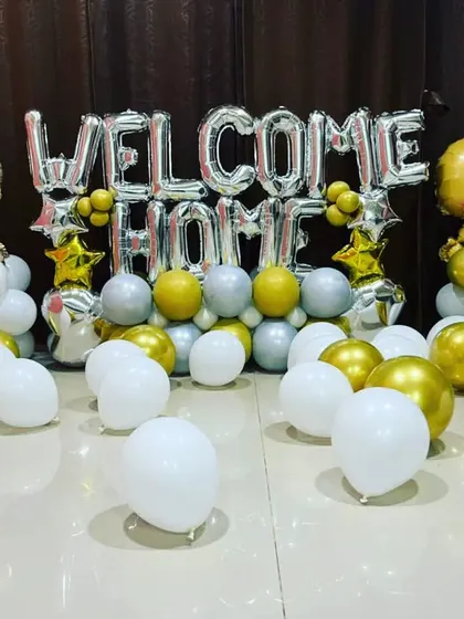 A sweet "Welcome Home" decoration for a newborn. The setup includes silver and gold balloons, with cute baby-shaped foil balloons on either side.