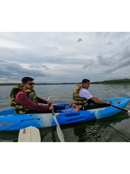 Two guests paddling in a double kayak, working together to explore the scenic lake on a cloudy day.