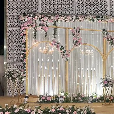 A beautiful stage backdrop featuring golden arches, hanging chandeliers, and cascading pink florals against a white curtain.