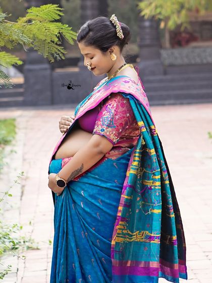 A side profile portrait showcasing the beautiful baby bump against the rich fabric of a Paithani saree. The traditional nath and jewelry complete the look perfectly.