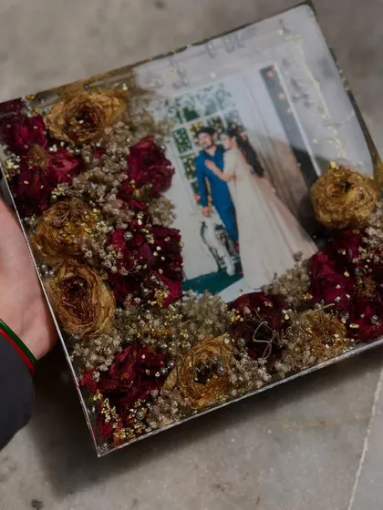 This square frame uses a mix of red roses and baby's breath to create a delicate border around the couple's wedding photo. The gold flakes add a touch of sparkle.