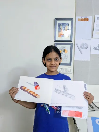 This student is holding her completed object studies, one in watercolor and the other in pencil. We encourage exploring the same subject in different mediums to understand how each can be used to show form and texture.