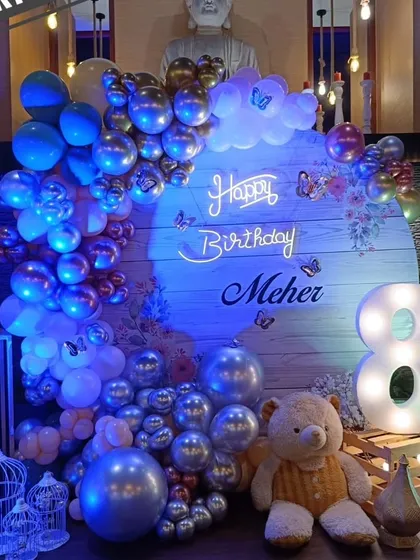 A beautiful blue and silver balloon arrangement for Meher's 8th birthday, featuring a wooden backdrop, a neon sign, and a cute teddy bear prop.
