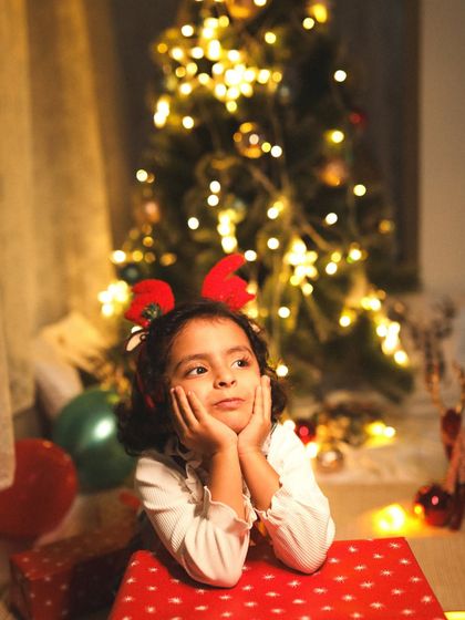 Waiting for Santa. This little girl's dreamy expression, lit by the warm glow of the Christmas tree, perfectly captures the magic of the holiday season.