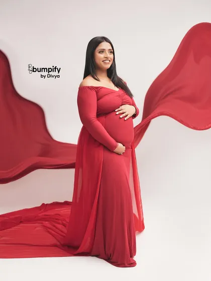 Looking off-camera, this pose creates a sense of wonder and anticipation. The flowing red fabric adds a touch of artistry to this beautiful maternity portrait.