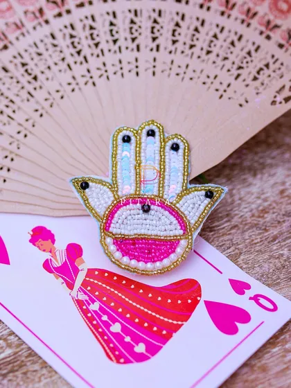 A close-up of the custom-designed stationery and favors, showing the intricate beadwork on the Hamsa brooch and the Queen of Hearts playing card.