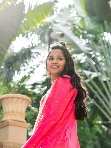 The bride shines in a vibrant pink outfit for one of her pre-wedding functions. Her hair is styled in a simple yet elegant half-updo with loose waves, a look that is both festive and easy to manage.