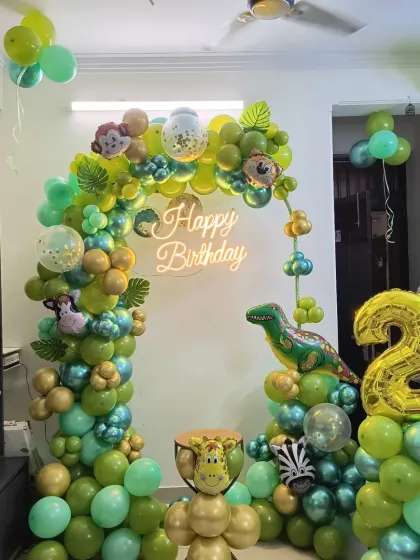 A lively dinosaur and jungle themed party for a second birthday. This home setup includes a green and gold balloon arch, a neon sign, and a large number '2' foil balloon.