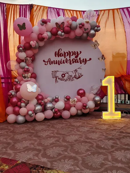 Celebrating a first anniversary with a custom backdrop in shades of pink and silver. This setup includes a personalized 'Happy Anniversary' graphic and a light-up number '1' to mark the special milestone.