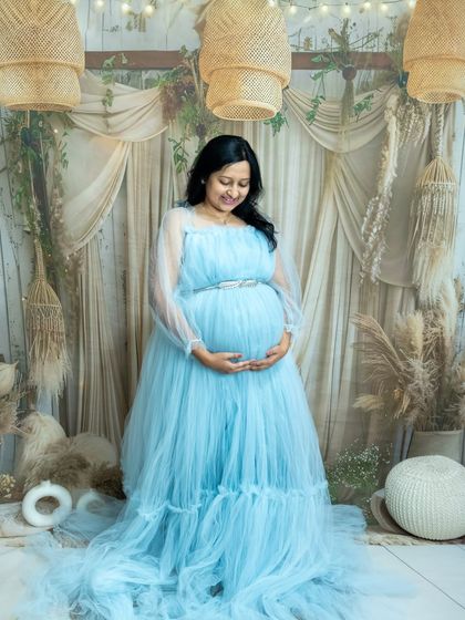 A serene studio portrait in our boho setup. The mom-to-be is wearing a beautiful light blue gown, looking peacefully at her baby bump.