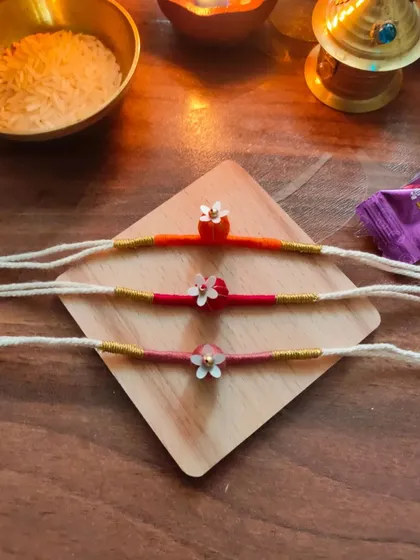 These delicate floral rakhis are handmade with thread and small beads. They come in a variety of warm colors like orange, pink, and red.