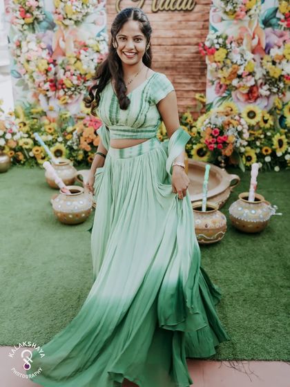 A full-length shot of the bride in her beautiful green Haldi outfit, smiling against a backdrop of sunflowers.