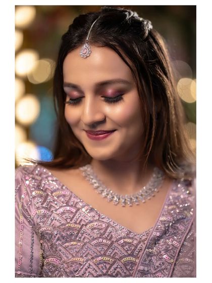 A serene bridal portrait with a soft, out-of-focus background. The focus is on her gentle smile, makeup, and delicate jewelry.
