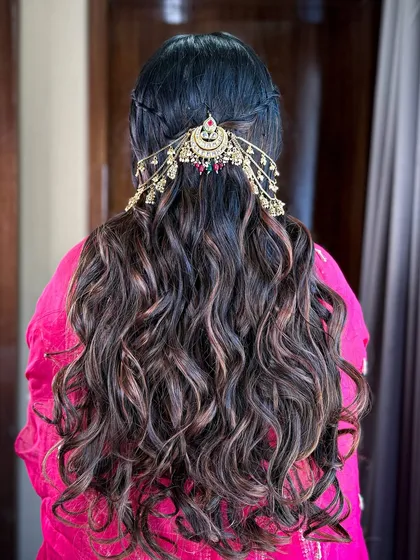 The hairstyle featured soft waves and a braided half-updo, decorated with a traditional, ornate hair accessory.