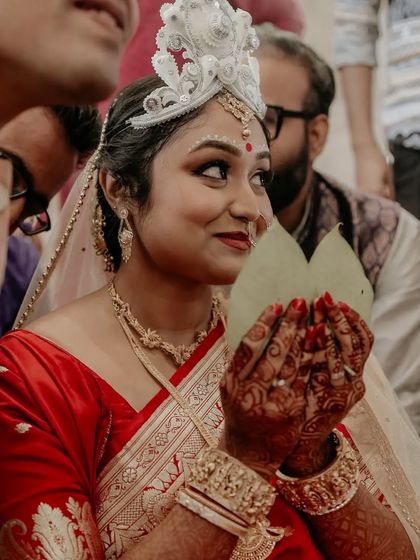 The bride during the "Shubho Drishti" ritual, holding betel leaves to cover her face before the big reveal.