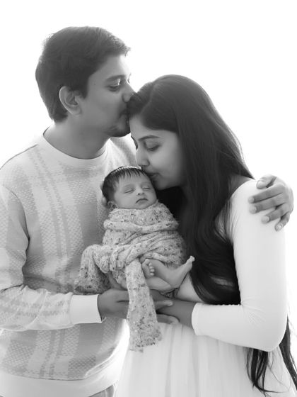 A classic high-key black and white portrait. The bright, airy feel brings all the focus to the family's gentle kisses and the sleeping baby they adore.