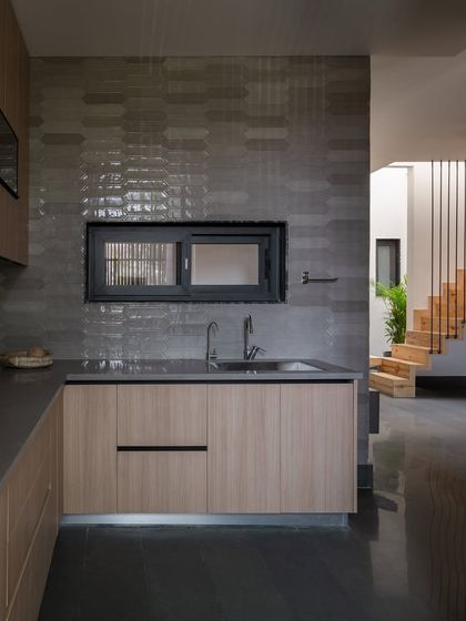 The open kitchen, with its light wood cabinetry and grey textured tiles, continues the home's minimal and functional aesthetic. A small window connects it to the light court, bringing in more daylight.