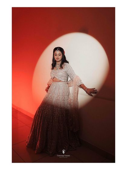 The bride posing in her ombre lehenga against a red-lit wall, creating a bold and dramatic reception portrait.