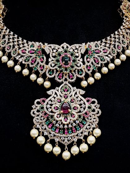This is a truly grand bridal necklace, heavily studded with American diamonds and colorful stones. The intricate floral design and pearl drops make it a showstopper piece for any bride.