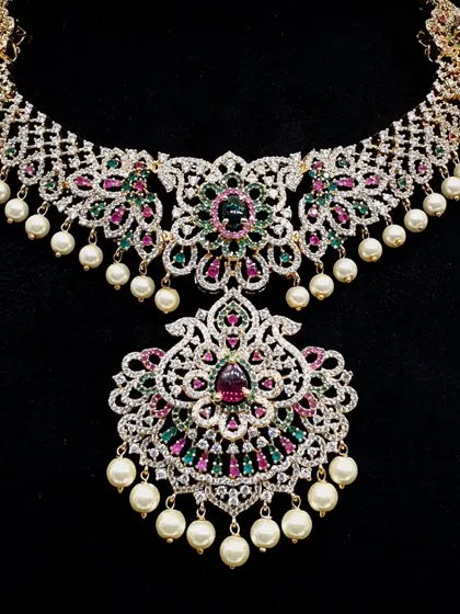 For a truly glamorous look, this heavy bridal necklace combines intricate AD stone work with colorful gems and pearls. It is a statement piece perfect for a grand reception or wedding ceremony.