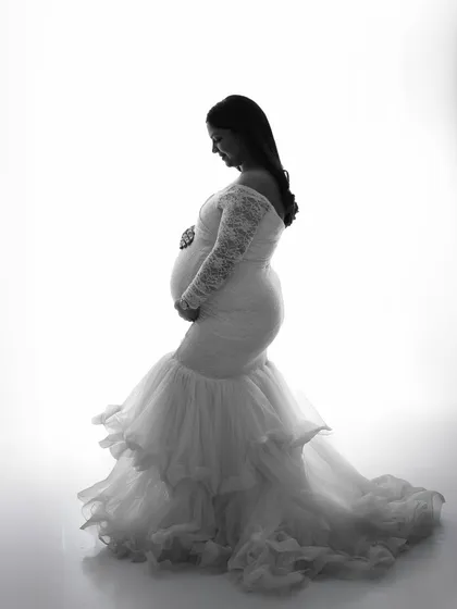 Silhouette photography creates timeless and dramatic portraits. This black and white image highlights the beautiful shape of pregnancy in a striking high-contrast style, using a delicate lace gown to add texture.