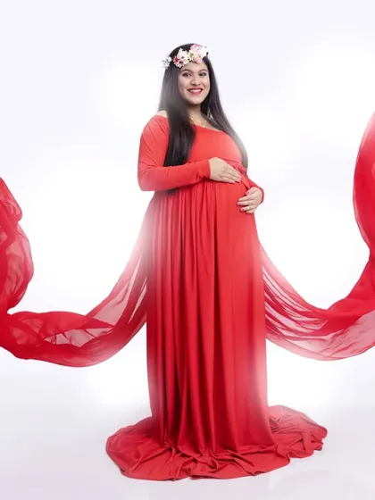 The vibrant red gown with its flowing fabric wings creates a striking visual against a clean white background. This is a powerful and confident look for any mom-to-be.