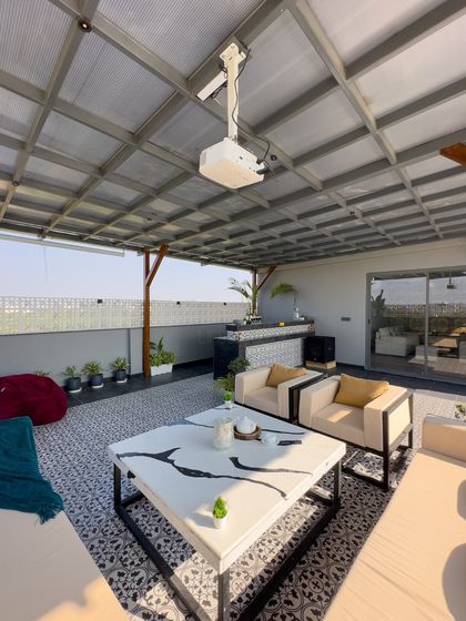 A view from inside a covered pergola, looking out over the terrace. This shot highlights the patterned tile floor, modern furniture, and the outdoor projector setup.
