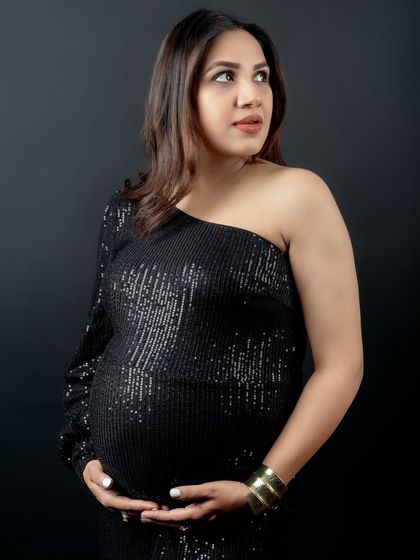 A beautiful close-up of the mom-to-be, looking away with a gentle expression. The studio lighting highlights the sparkle of her dress and her natural pregnancy glow.