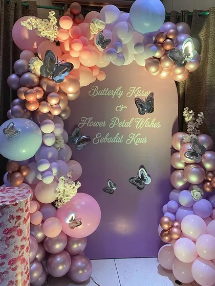 An elegant butterfly-themed backdrop in pastel pink and purple. The custom text reads "Butterfly Kisses & Flower Petal Wishes", adding a poetic touch to the celebration.